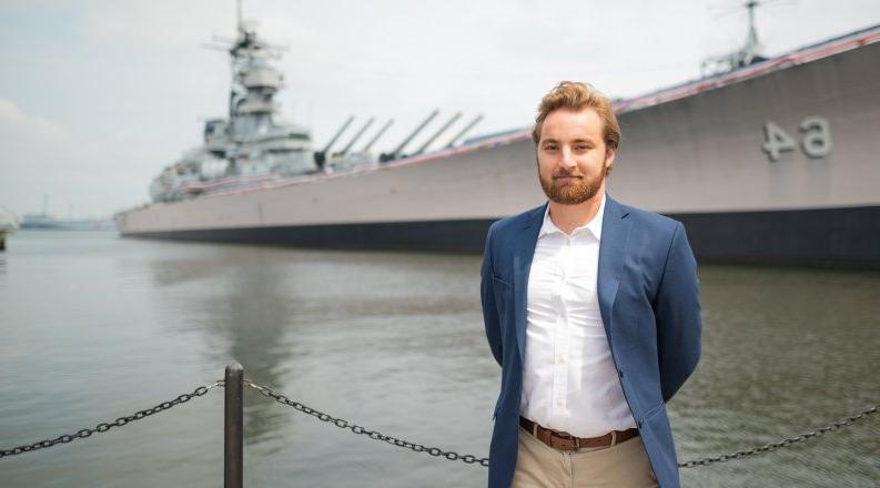 A young man stands on a pier by the Battleship 威斯康辛州 in Nofolk.